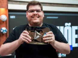 Casimiro Miguel, criador da CazéTV, sorrindo e segurando placa do YouTube em estúdio esportivo durante gravação de conteúdo digital.