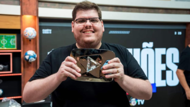 Casimiro Miguel, criador da CazéTV, sorrindo e segurando placa do YouTube em estúdio esportivo durante gravação de conteúdo digital.
