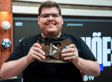 Casimiro Miguel, criador da CazéTV, sorrindo e segurando placa do YouTube em estúdio esportivo durante gravação de conteúdo digital.