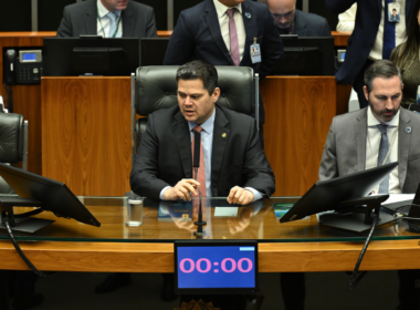 Imagem mostra Davi Alcolumbre presidindo sessão no Senado Federal em Brasília. O parlamentar aparece na mesa diretora do Congresso Nacional cercado por assessores e outros políticos durante debate envolvendo a CPI do Banco Master. A cena retrata o ambiente político institucional brasileiro, com destaque para o plenário e os equipamentos utilizados nas sessões legislativas.