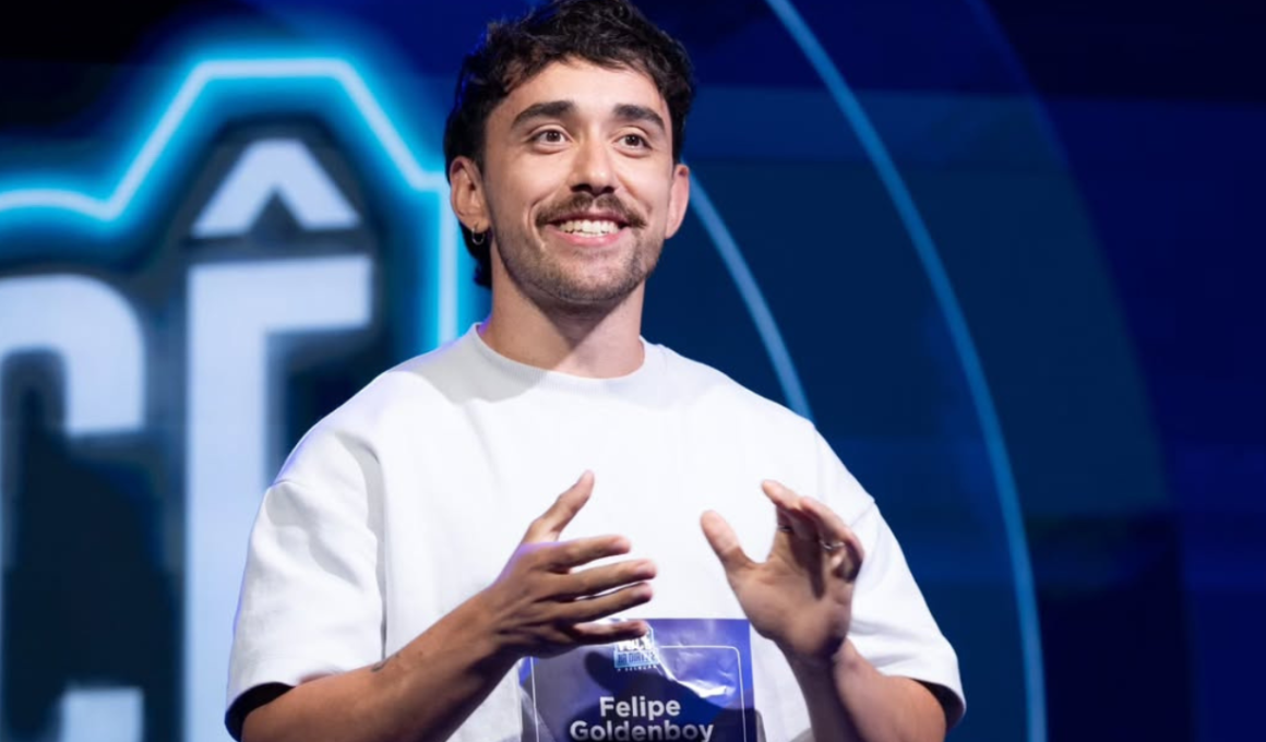 Felipe Goldenboy durante participação em programa da DiaTV. Na imagem, o jornalista, streamer e criador de conteúdo digital aparece em um estúdio com iluminação em tons de azul, usando camiseta clara e demonstrando expressão descontraída enquanto fala ao público. Conhecido por sua atuação no universo gamer, cultura pop e entretenimento online, Felipe Goldenboy ganhou destaque nas redes sociais e na plataforma DiaTV por conteúdos voltados à geração jovem e ao cenário digital brasileiro.