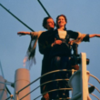 Cena icônica do filme Titanic com casal na proa do navio, braços abertos ao vento durante pôr do sol, simbolizando romance e liberdade.