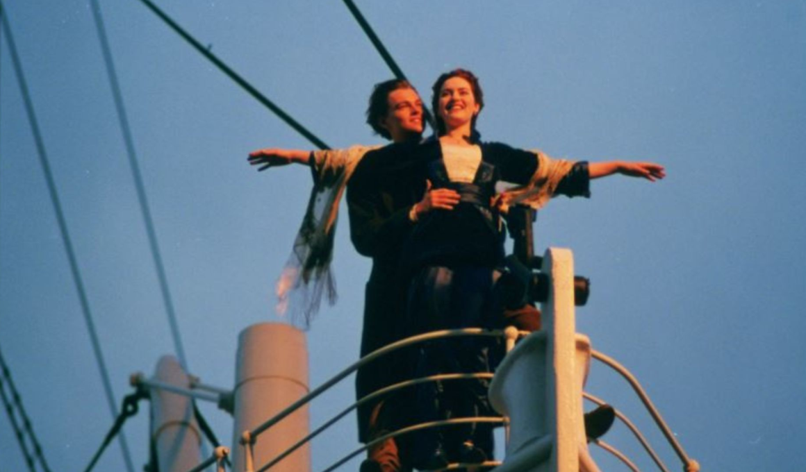 Cena icônica do filme Titanic com casal na proa do navio, braços abertos ao vento durante pôr do sol, simbolizando romance e liberdade.