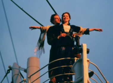 Cena icônica do filme Titanic com casal na proa do navio, braços abertos ao vento durante pôr do sol, simbolizando romance e liberdade.