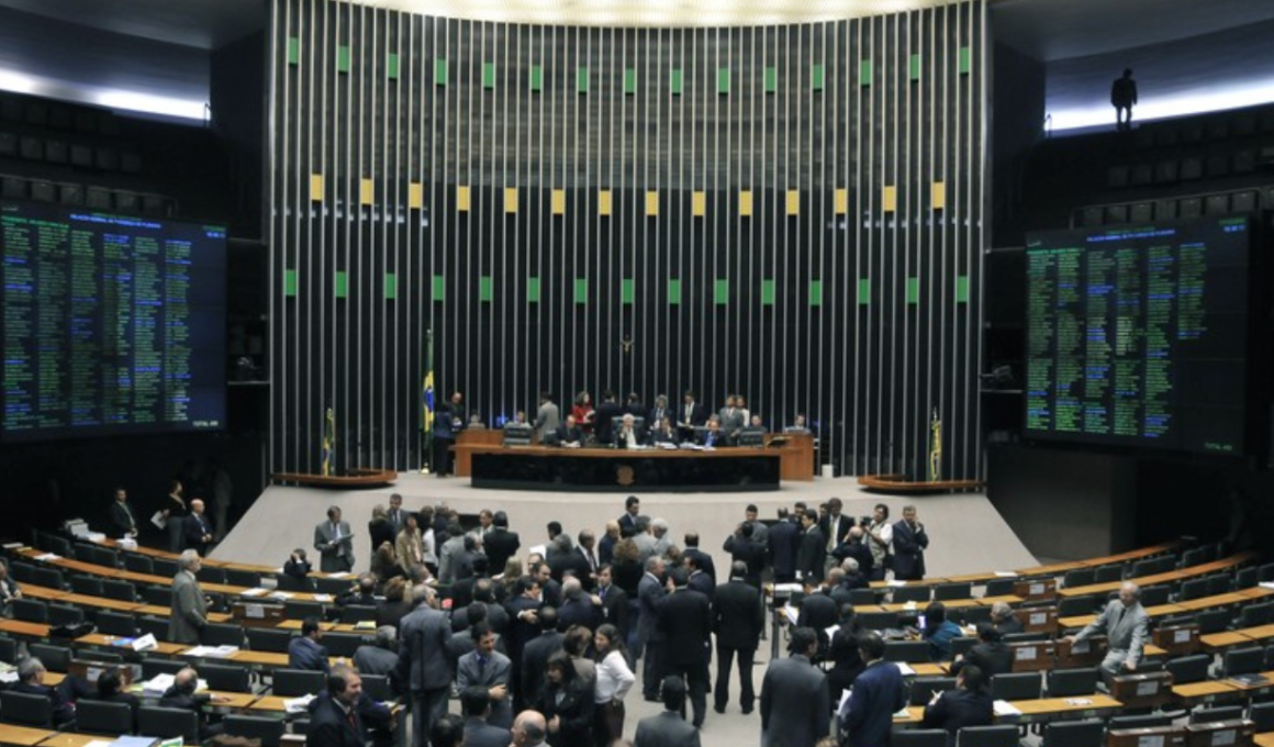 Vista geral do Plenário Ulysses Guimarães na Câmara dos Deputados, em Brasília, mostrando deputados federais reunidos em sessão com os painéis eletrônicos de votação acesos ao fundo.