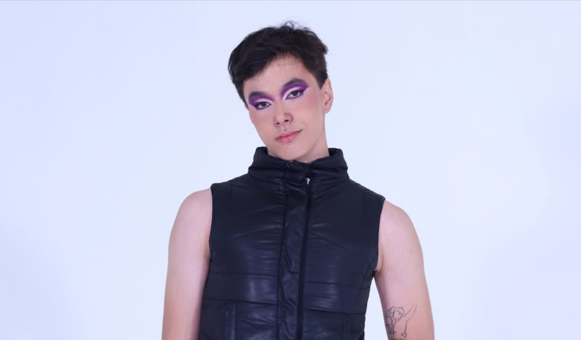 Retrato da streamer e criadora de conteúdo Veronika Volt, posando de frente contra um fundo branco. Ela exibe uma maquiagem artística nos olhos em tons de roxo e lilás com delineado gráfico branco e preto. Veste um colete preto acolchoado de gola alta, deixando os braços à mostra, onde é possível ver uma tatuagem de querubim no braço esquerdo.