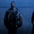 Foto promocional do clipe "Mi Chico" mostrando a cantora Melody de perfil, o cantor Jason Derulo ao centro sem camisa com jaqueta preta de látex, e o DJ Goja à direita vestindo moletom preto. O ambiente é escuro, com tons frios e névoa cenográfica.