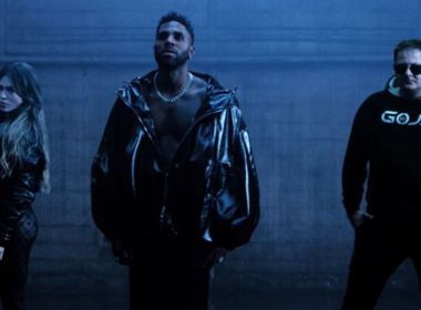 Foto promocional do clipe "Mi Chico" mostrando a cantora Melody de perfil, o cantor Jason Derulo ao centro sem camisa com jaqueta preta de látex, e o DJ Goja à direita vestindo moletom preto. O ambiente é escuro, com tons frios e névoa cenográfica.