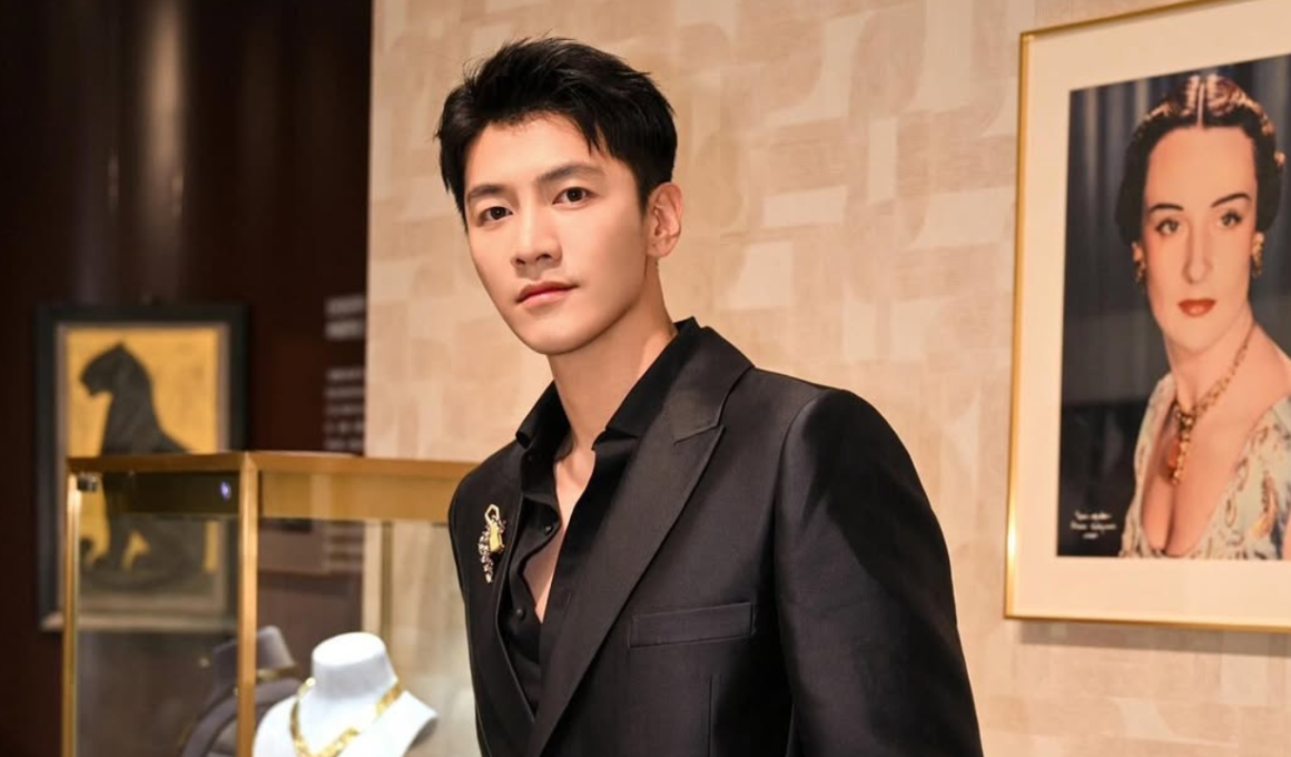 Ator chinês Jin Ze posa usando terno preto elegante em ambiente sofisticado, durante evento ligado ao universo dos doramas. O artista aparece em destaque diante de obras de arte e decoração de luxo.