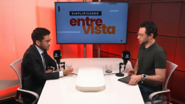 Kim Kataguiri participa de entrevista no programa Simplificando, da DiaTV, conduzida por Gui Sampaio. O deputado federal aparece à esquerda, de terno e gravata, enquanto o apresentador está à direita, em frente aos microfones, em um estúdio com iluminação vermelha e um monitor ao fundo exibindo a identidade visual do programa "Simplificando Entrevista".