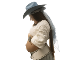 Lauana Prado posa de perfil exibindo a barriga de gravidez em ensaio fotográfico com fundo branco, usando chapéu azul-claro, blusa branca rendada e saia clara, em anúncio do nascimento do primeiro filho e lançamento de nova música.