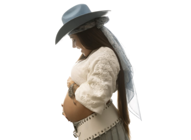 Lauana Prado posa de perfil exibindo a barriga de gravidez em ensaio fotográfico com fundo branco, usando chapéu azul-claro, blusa branca rendada e saia clara, em anúncio do nascimento do primeiro filho e lançamento de nova música.
